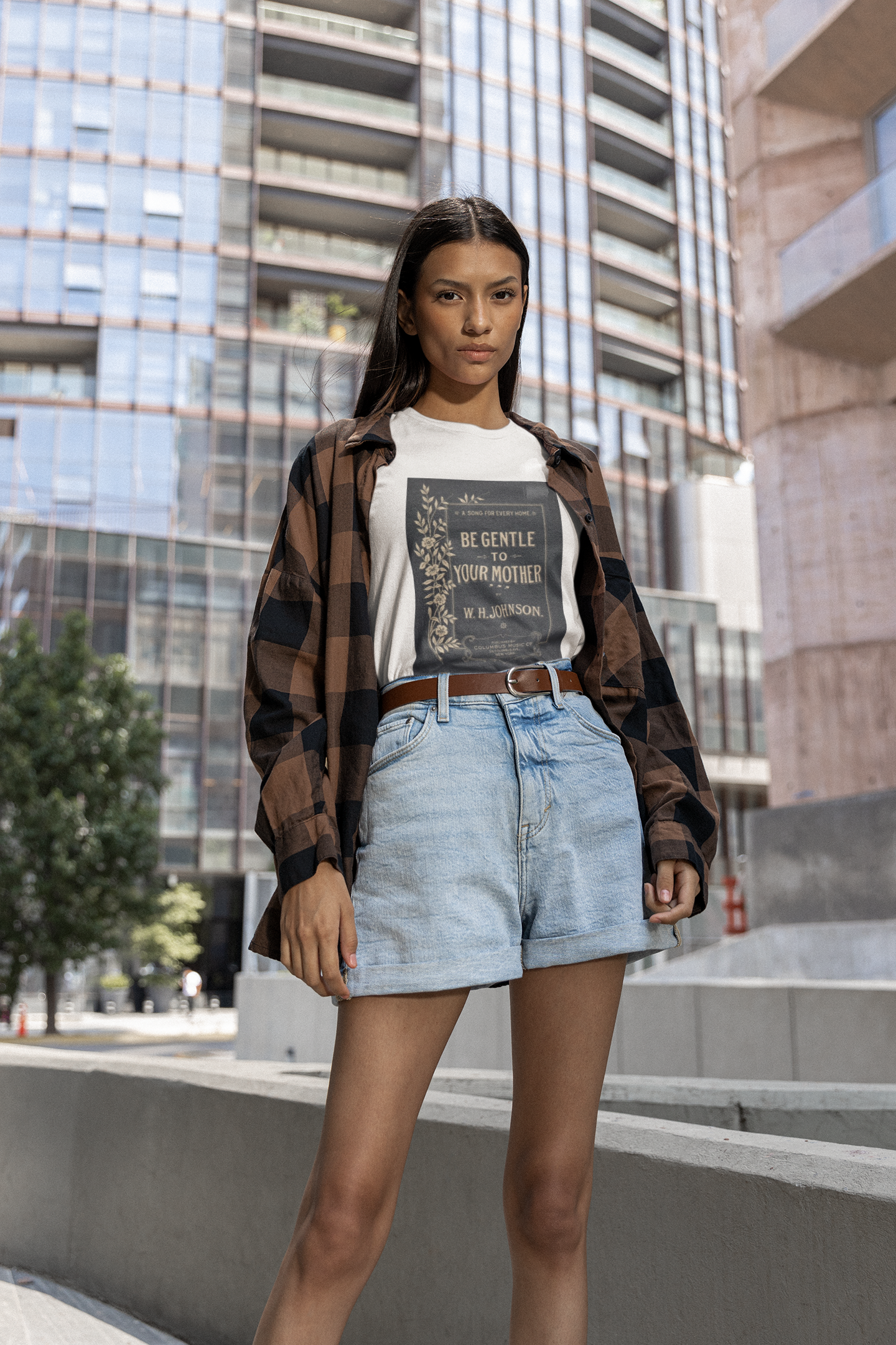 Woman in urban background wearing streetwear outfit consisting of a white t shirt with a large black print of the vintage album cover be gentle to your mother