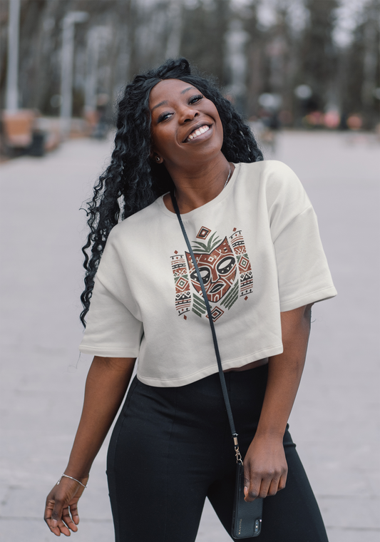 Woman wearing a white crop top with an intricate Aztec tribal mask print, smiling outdoors.